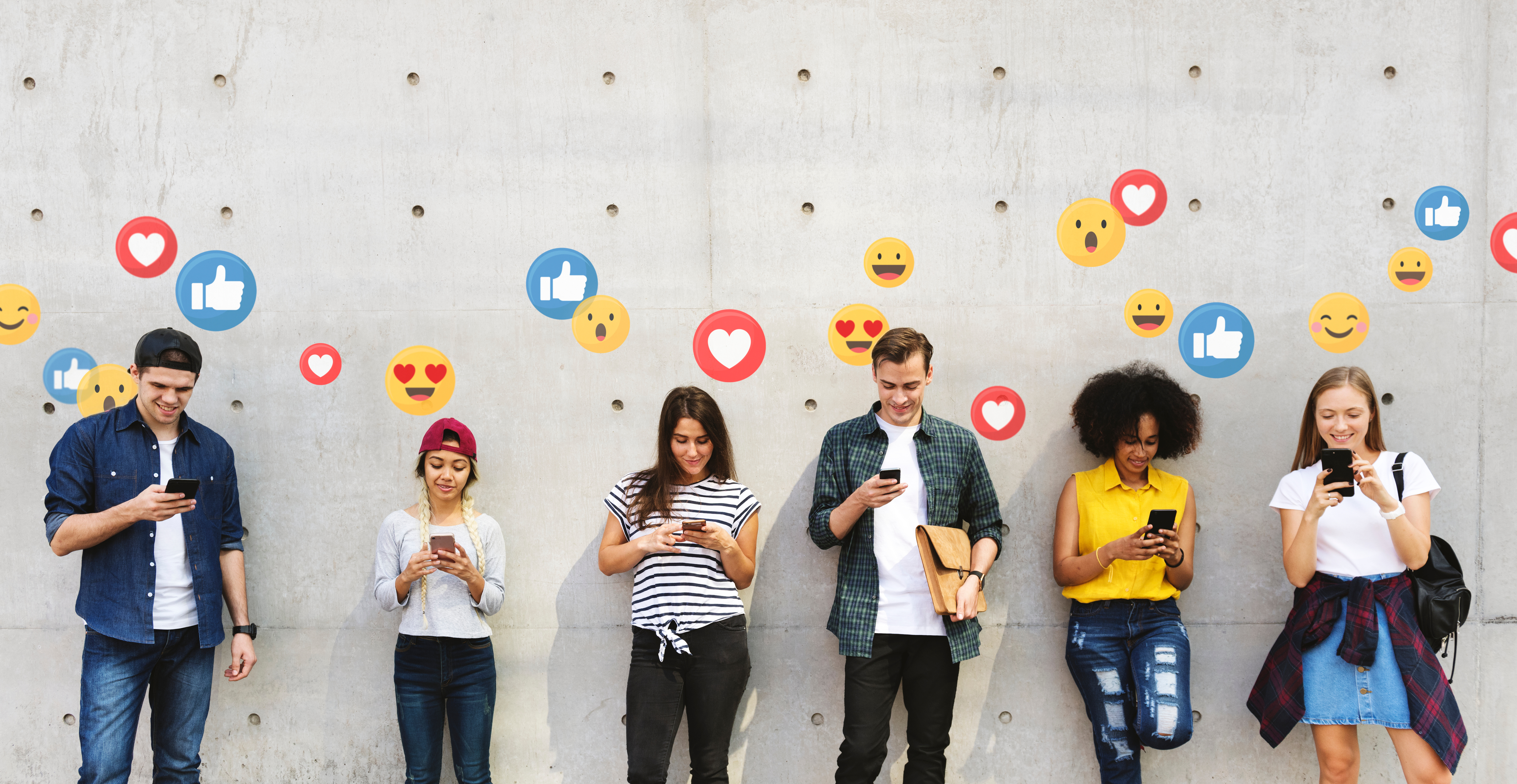 6 junge Menschen stehen vor einer Mauer. Sie schauen auf ihre Handys. Über den Handys sind Social Media Icons wie Emojis, Herzen und Daumen hoch zusehen.
