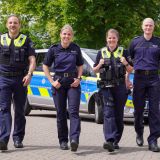 Two female and two male police officers walk away from a patrol car and present the new dark blue polo shirts