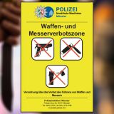 Gelbes Schild der neuen Waffenverbotszone mit durchgestrichenen Waffen und Messern