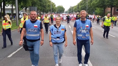 Zwei Polizisten aus Polen und eine deutsche Polizistin führen lächelnd eine große Gruppe polnischer Fans an.