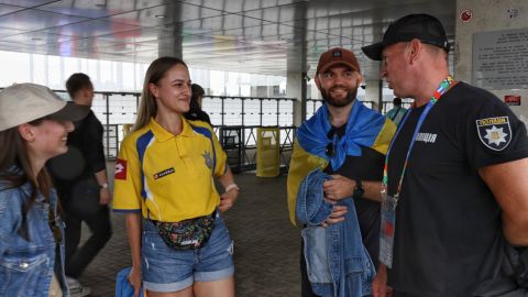 Ukrainischer Polizist unterhält sich mit ukrainischen Fans, die blau-gelbe Trikots und Fahnen tragen.