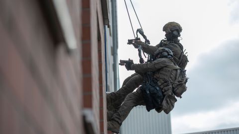 Zwei SEK-Beamte des Klettertrupps seilen sich außen an einer Hauswand in ein Fenster ab. Sie halten ihre Waffen in den Raum gerichtet.